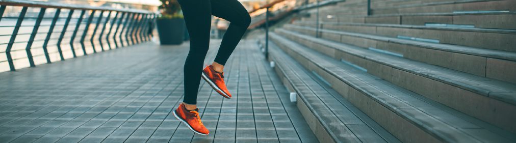 Mobility Exercises. Two legs in running shoes are suspended mid-air ready to run up a set of cement stairs.